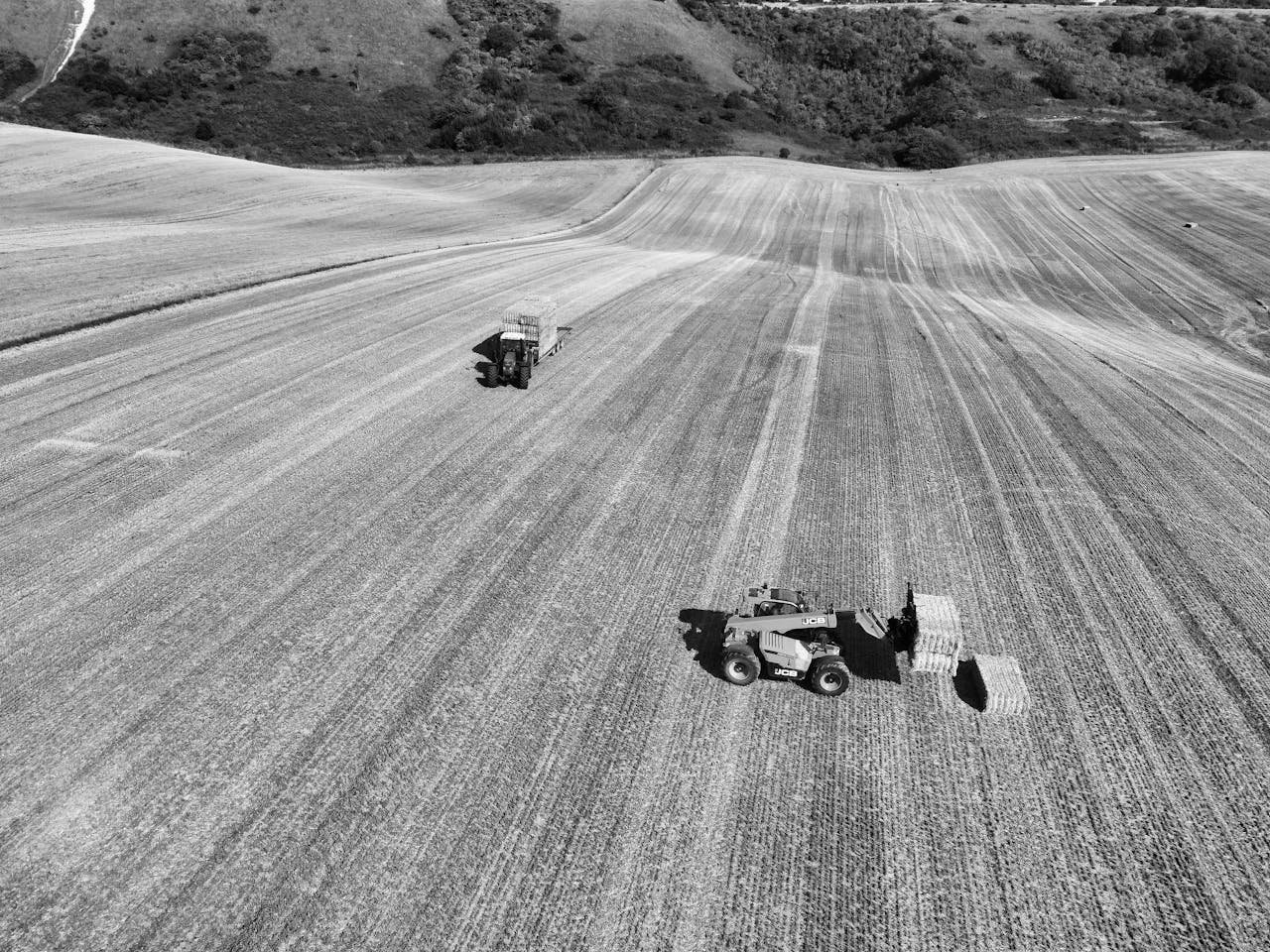 Black and white aerial view of farming machinery in an English field highlighting rural agriculture.